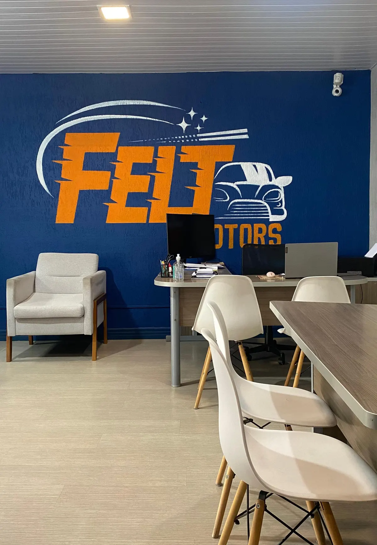 Sala de atendimento da Felt Motors, com mesa, cadeiras e o logo na parede azul